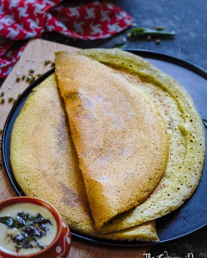 Pesarattu or green gram dosa served on a black plate with a bowl of coconut chutney