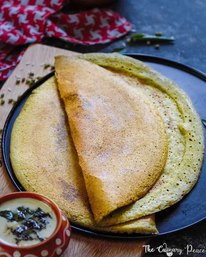 Pesarattu or green gram dosa served on a black plate with a bowl of coconut chutney