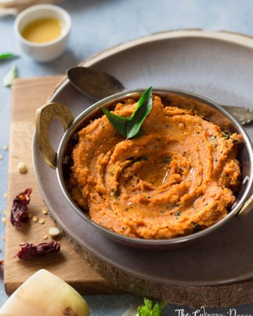 Orange coloured radish or moolangi chutney served in a bowl with curry leaves and placed against a light background