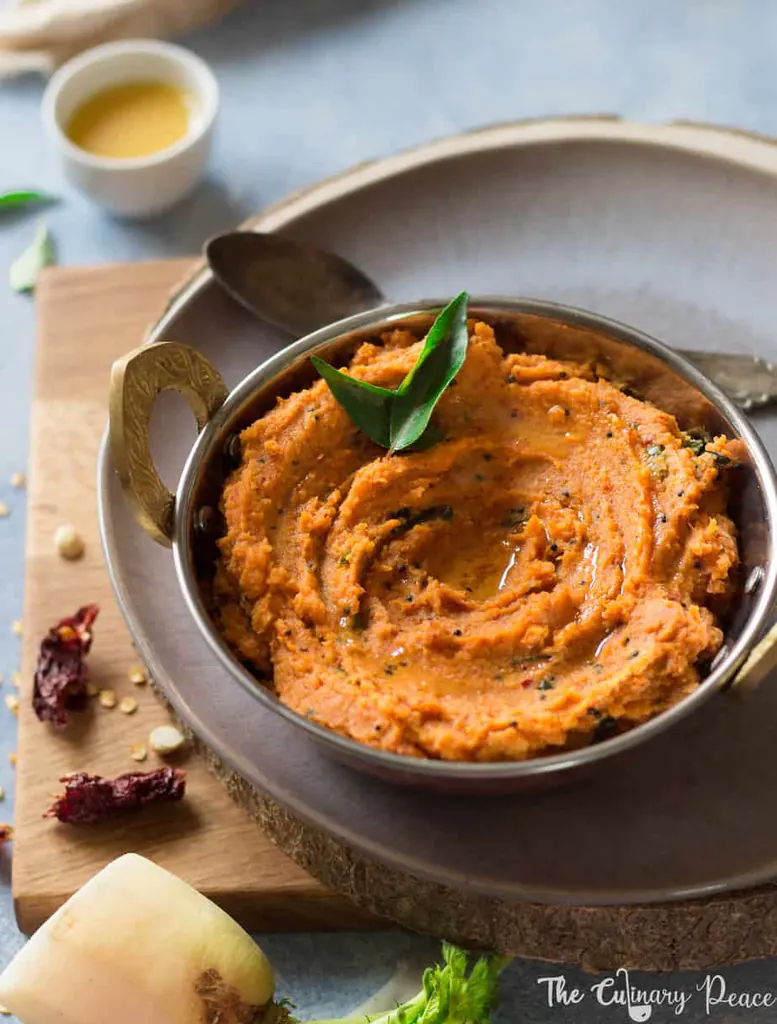 Orange coloured radish or moolangi chutney served in a bowl with curry leaves and placed against a light background